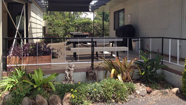 A covered patio area with a table and chairs, surrounded by potted plants and a statue. - Boggabilla Motel (Boggabilla)