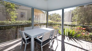 Un porche cubierto con una mesa y sillas, con vistas a un jardín y una casa.