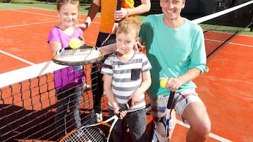 Un court de tennis avec un filet, des palmiers et une maison en arrière-plan.