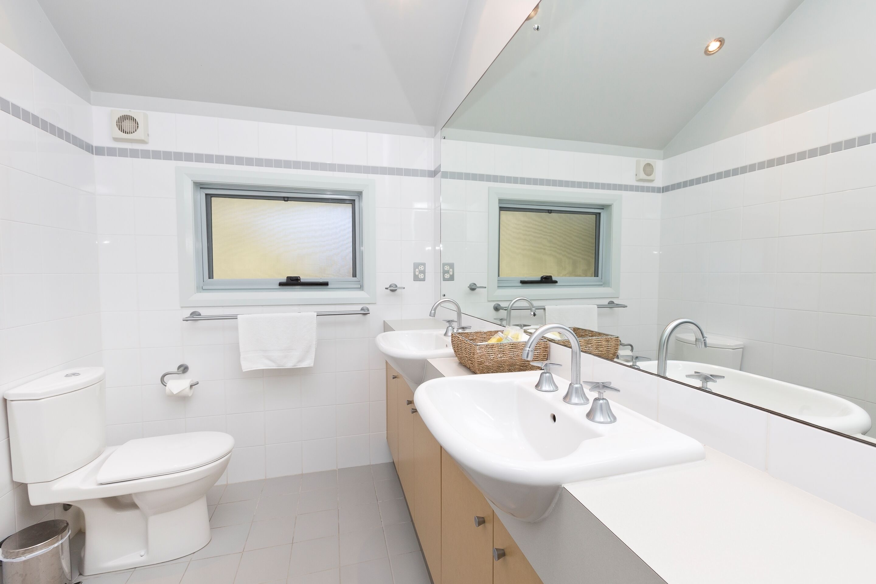 A modern bathroom with a toilet, two sinks, a large mirror, and a window.