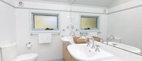 A modern bathroom with a toilet, two sinks, a large mirror, and a window.