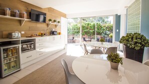 A modern kitchen with white cabinets, a built-in TV, and a dining area with a glass table and chairs. - Crown Hotel Surry Hills (Surry Hills)