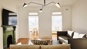 A living room with a fireplace, a sofa, a television, and a dining area with chairs and a table. - Crown Hotel Surry Hills (Surry Hills)