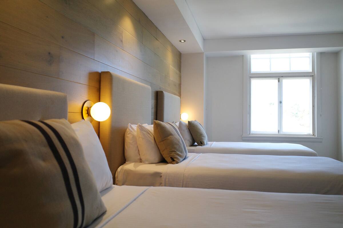 Une chambre d’hôtel avec deux lits, des têtes de lit en bois et des lampes fixées au mur.