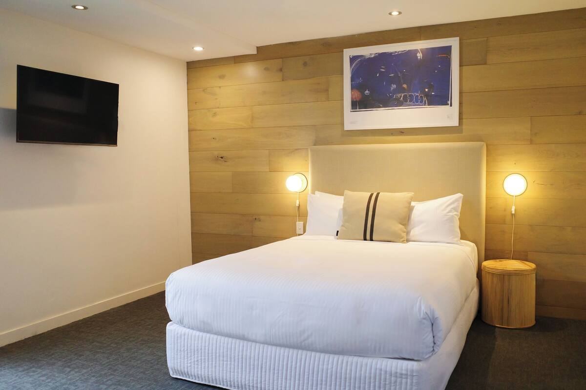 Une chambre d’hôtel avec un grand lit, des murs lambrissés en bois, un téléviseur fixé au mur et deux lampes de chevet.