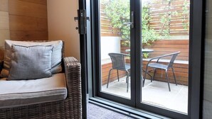 A wicker sofa with a cushion and a sliding glass door leading to an outdoor patio with two chairs and a table. - Crown Hotel Surry Hills (Surry Hills)