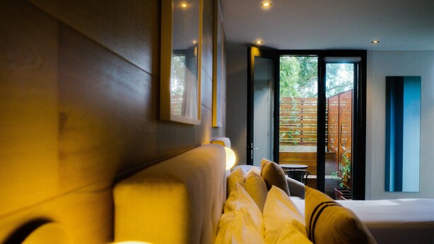 A modern hotel room with a large bed, a bedside table, and a view of the outdoor area through a sliding glass door. - Crown Hotel Surry Hills (Surry Hills)