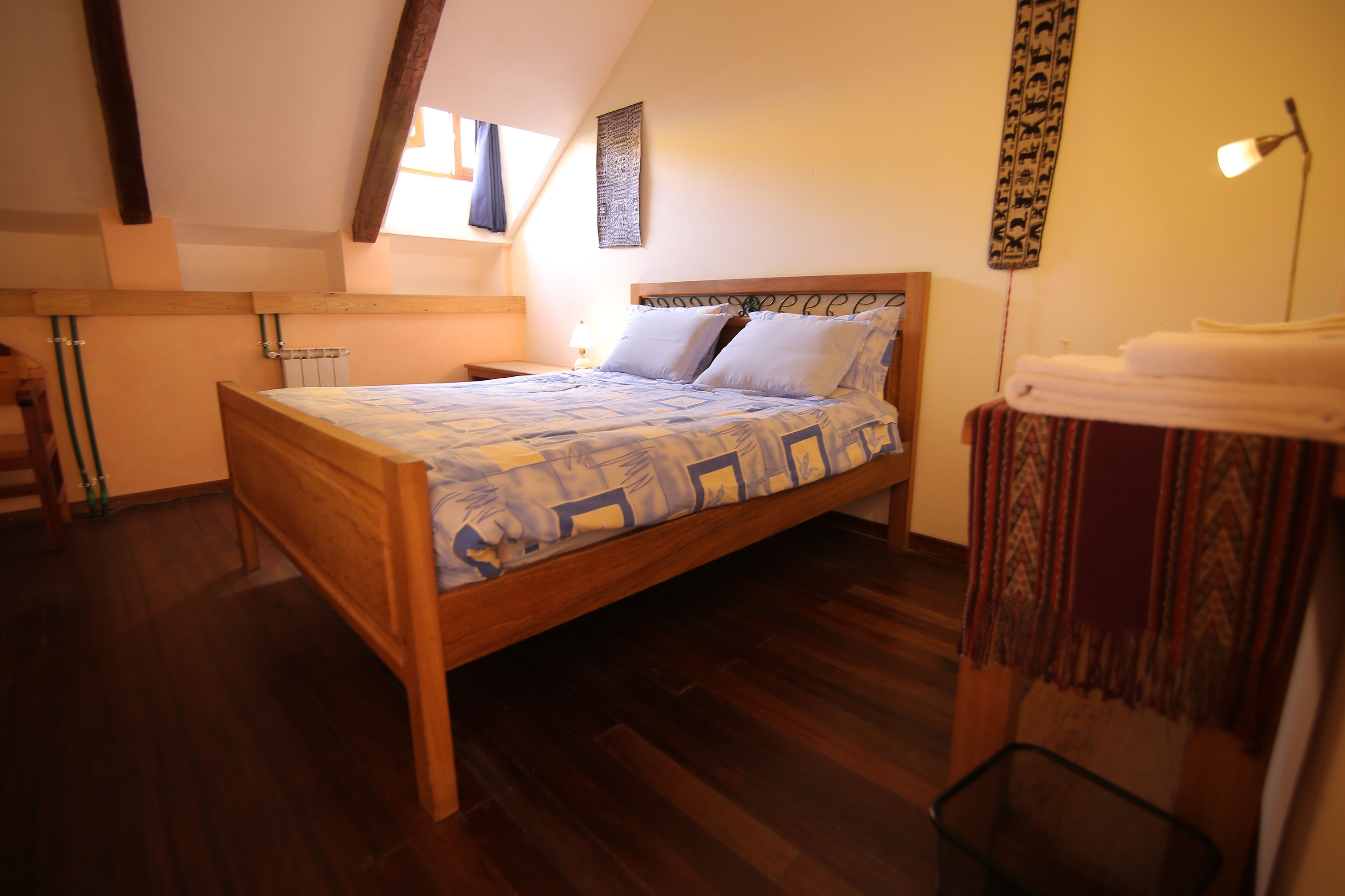 A bedroom with a wooden bed, a radiator, a window with curtains, and a wall-mounted artwork.