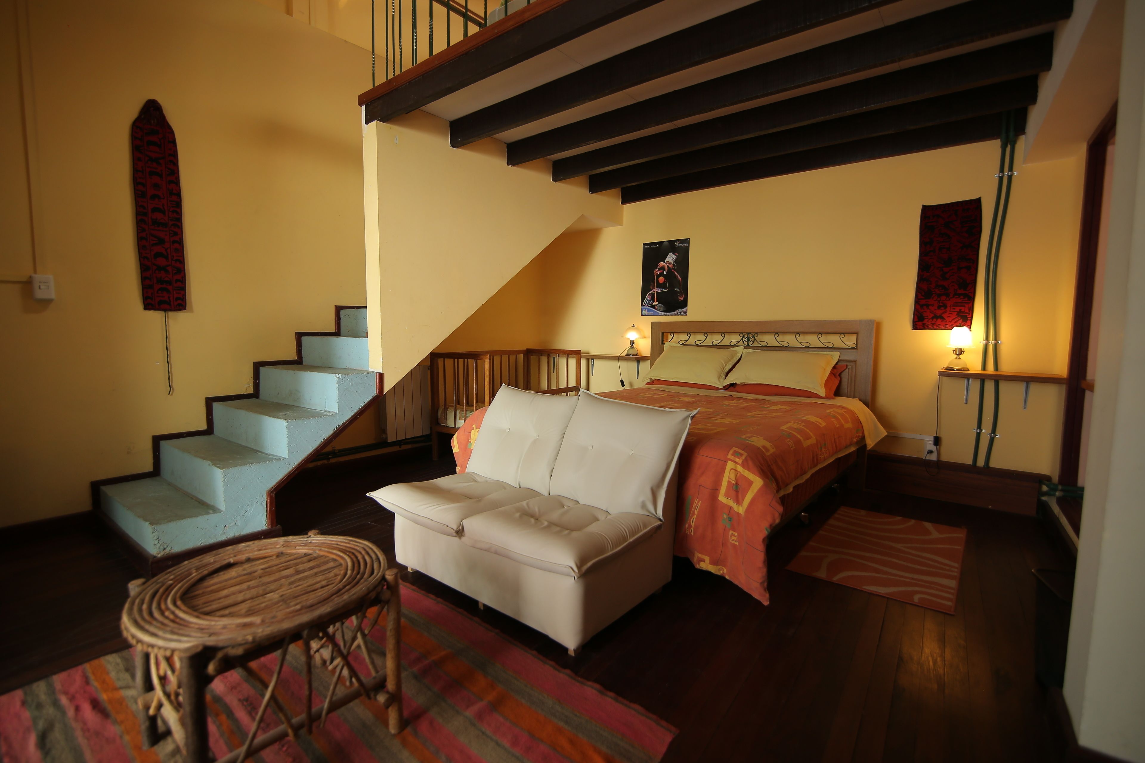 Un dormitorio con cama, sofá, sillón, escalera y un tapiz colgado en la pared.
