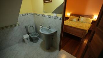 A bathroom with a toilet, sink, and a bed with a wooden headboard.