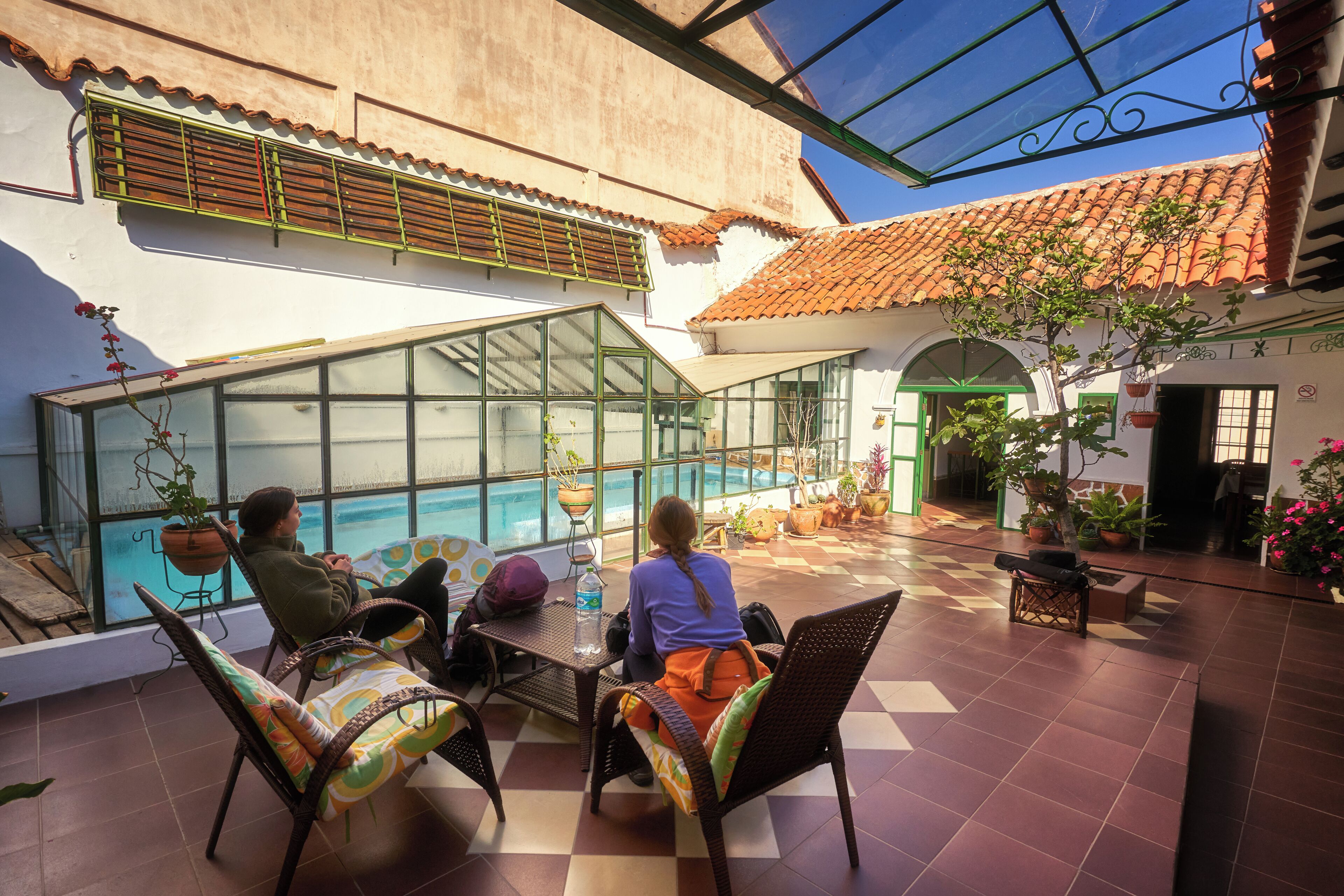 Une terrasse extérieure dotée d’une véranda en verre, de sièges et de plantes en pot.