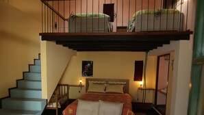 Un dormitorio con una cama litera, un sofá, una silla de mimbre, un felpudo a rayas, una escalera y un baño con espejo.