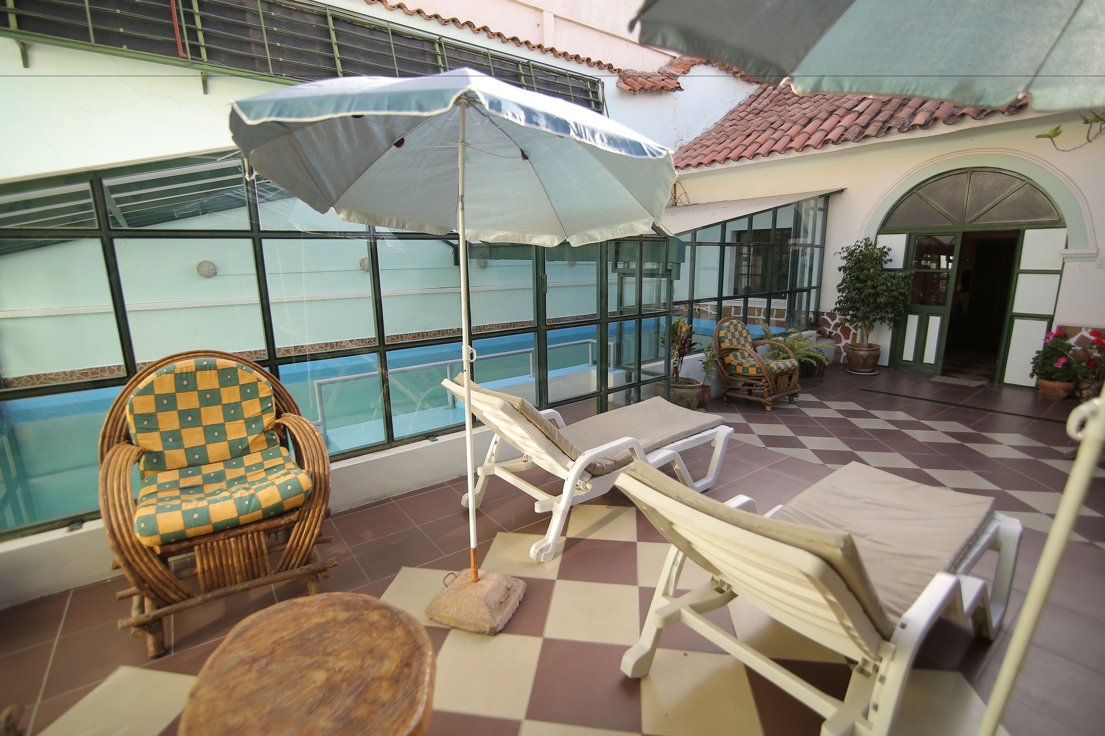 A sunlit indoor patio with a pool, lounge chairs, and a checkered chair.