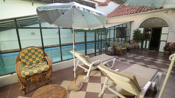A sunlit indoor patio with a pool, lounge chairs, and a checkered chair.