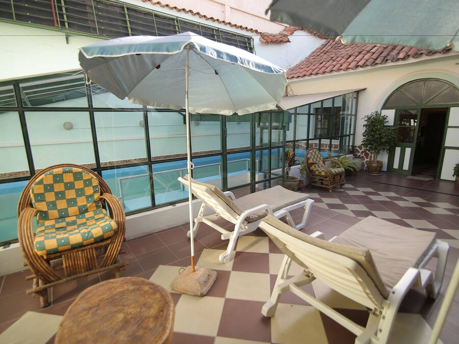 A sunlit indoor patio with a pool, lounge chairs, and a checkered chair.