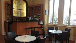 A bar area with a stained glass window, wooden shelves with bottles, and two round tables with chairs. - Le Métropole (Luxeuil-les-Bains)