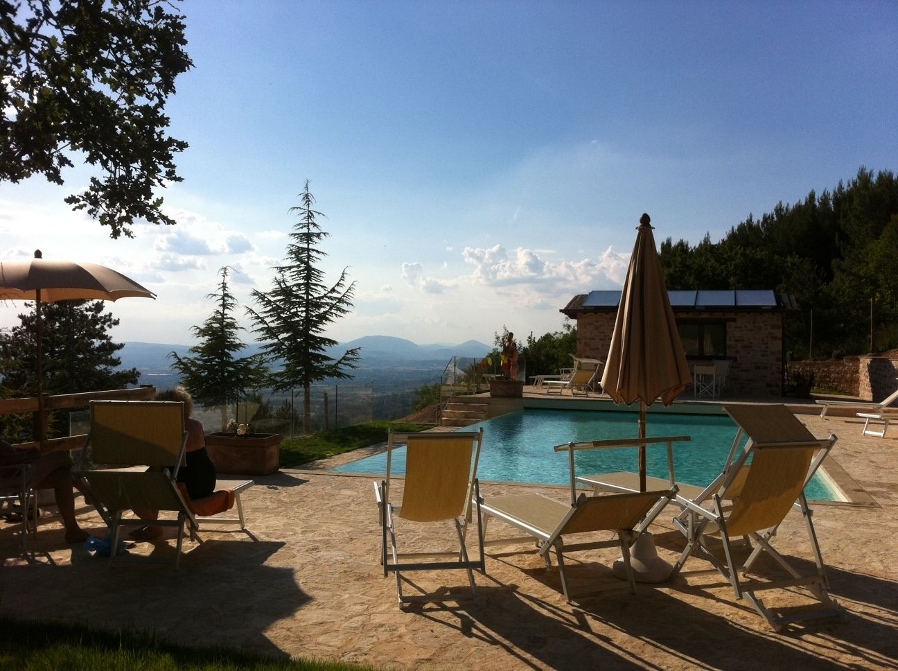 Zona de piscina con sillones de descanso y sombrillas, con vistas a un paisaje montañoso.