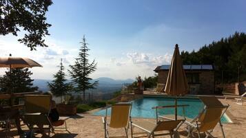 Zona de piscina con sillones de descanso y sombrillas, con vistas a un paisaje montañoso.