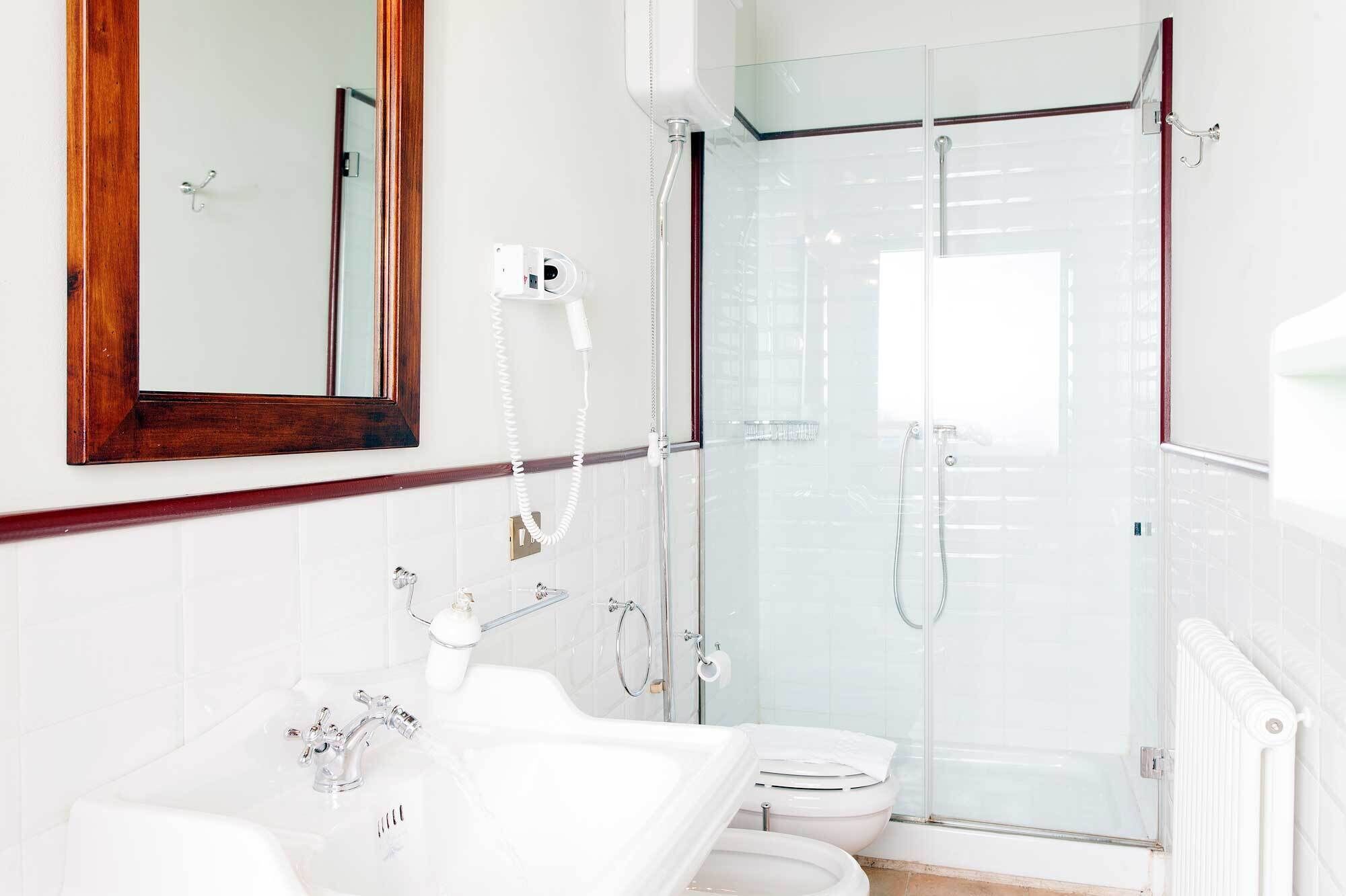 A modern bathroom with a glass shower enclosure, a white sink, and a wooden-framed mirror.