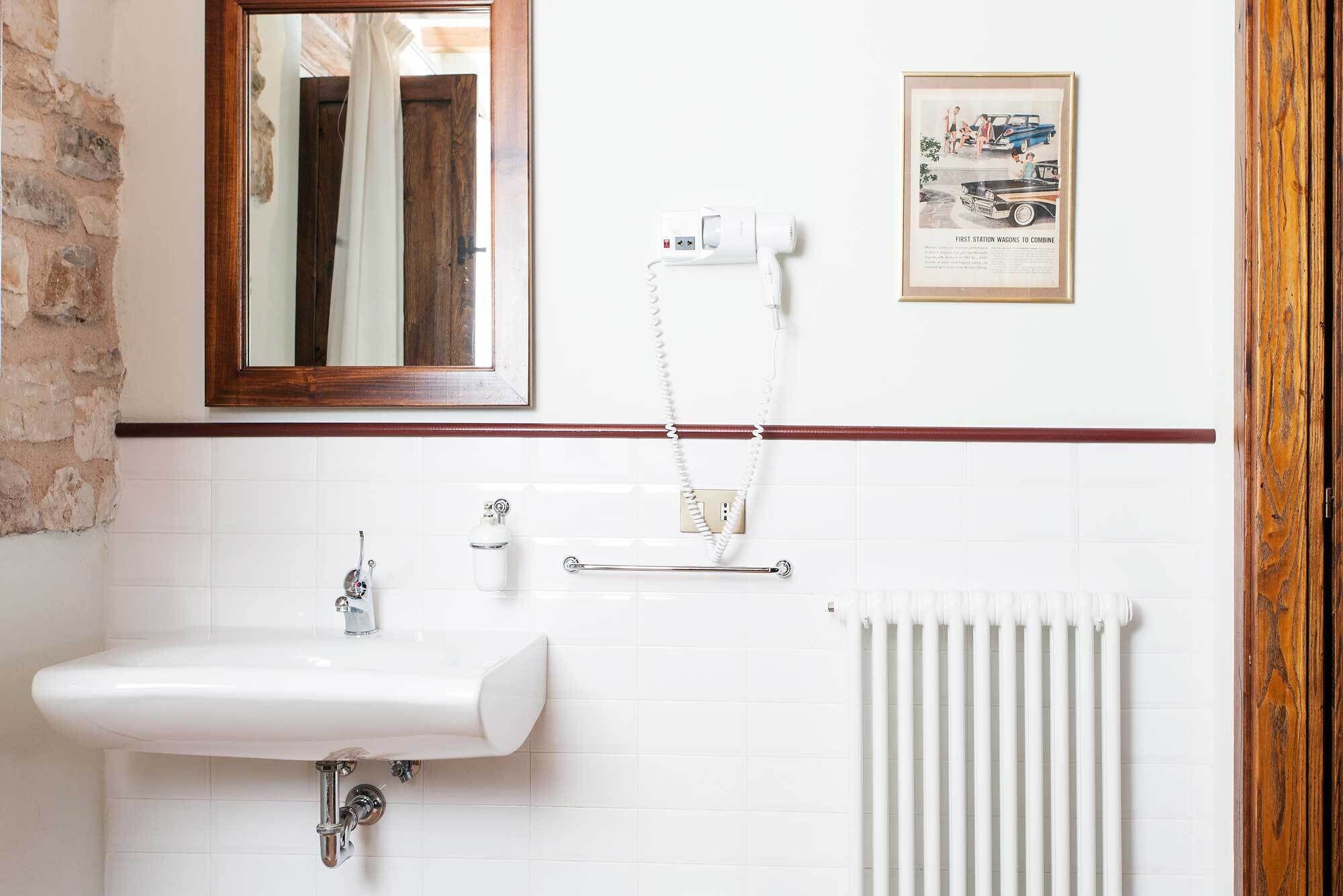 A bathroom with a white sink, a mirror, a radiator, and a framed picture on the wall.