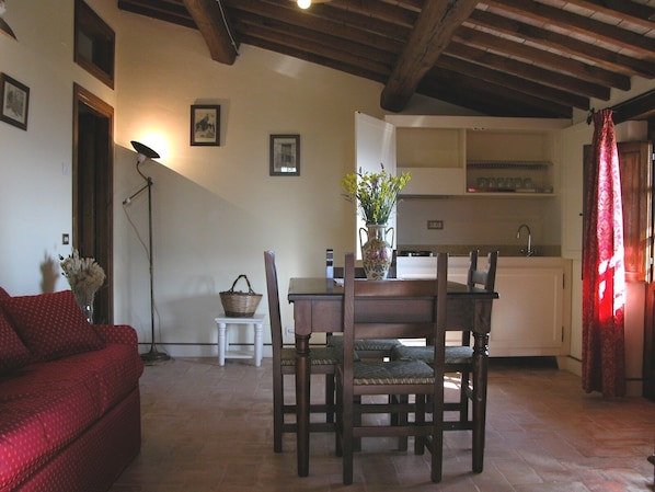 A cozy living room with a red sofa, wooden dining table, and chairs. A vase with flowers is on the table.