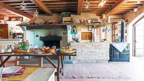 A rustic kitchen with a brick fireplace, wooden beams, and a dining area with a table set for two.