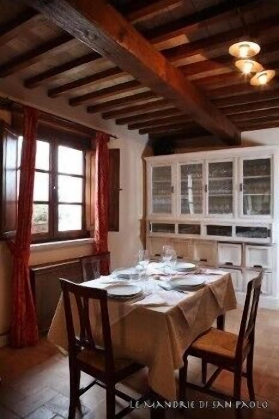 A dining room with a table set for four, wooden chairs, a window with red curtains, and a cabinet with glass doors.