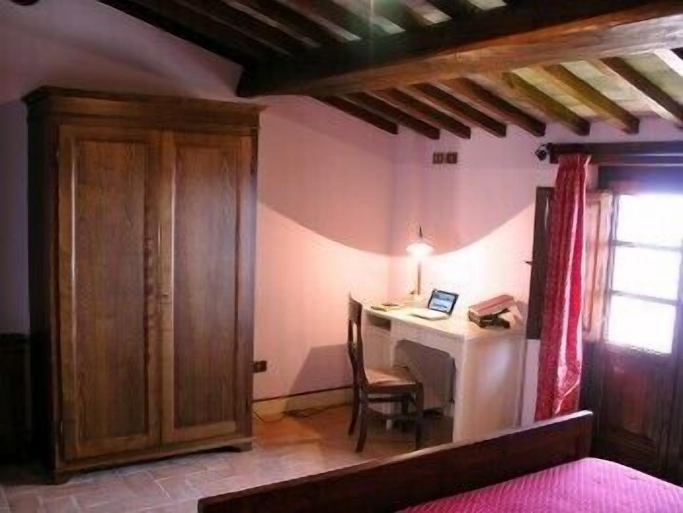 Un dormitorio con un armario de madera, un escritorio con silla, una cama y una ventana con cortinas.