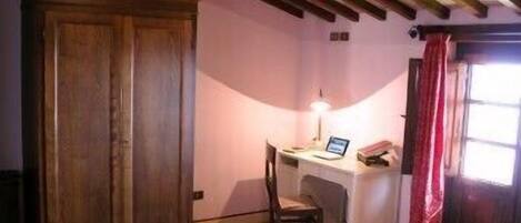 Un dormitorio con un armario de madera, un escritorio con silla, una cama y una ventana con cortinas.