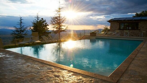 A swimming pool with a view of the sunset, surrounded by lounge chairs and trees.