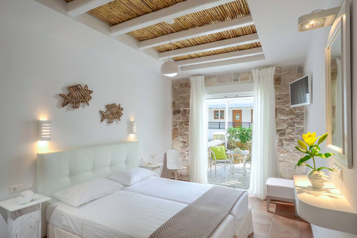 Une chambre d’hôtel moderne dotée d’un grand lit, d’un mur en pierre, d’un balcon avec coin salon extérieur et d’une vue sur la mer.