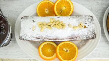 A dessert plate with a rectangular cake dusted with powdered sugar, surrounded by orange slices and almonds.