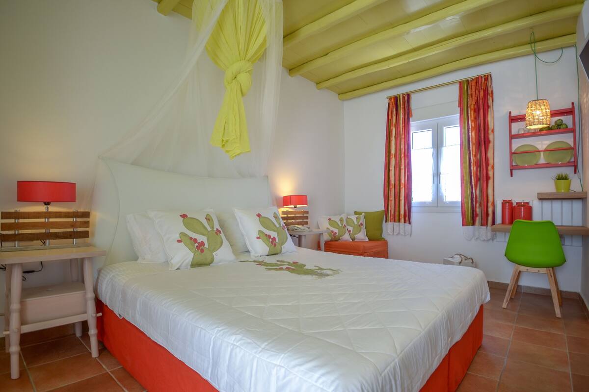 Une chambre à coucher comprenant un lit, des tables de chevet, une chaise, une étagère avec des objets décoratifs et une fenêtre avec des rideaux.