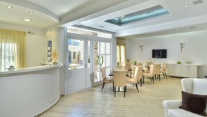 A spacious hotel lobby with a reception desk, dining area, and a large window offering a view of the outside. - Adriani Hotel (Naxos)