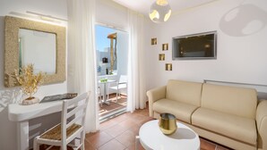 A modern living room with a sofa, a dining table, and a TV mounted on the wall. - Adriani Hotel (Naxos)