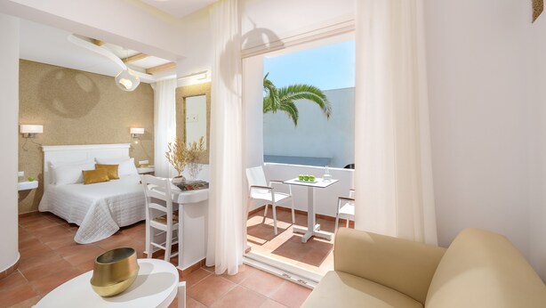 A hotel room with a bed, a small table with chairs, a balcony with a view of the sea, and a window with curtains. - Adriani Hotel (Naxos)