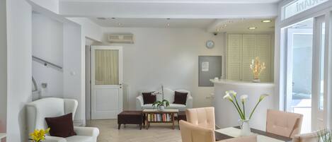 A modern living room with a white sofa, a coffee table with books, and a dining area with chairs.
