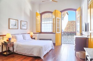 Habitación de hotel con cama, lámparas de noche, una mesita y vistas al exterior a través de una puerta abierta.
