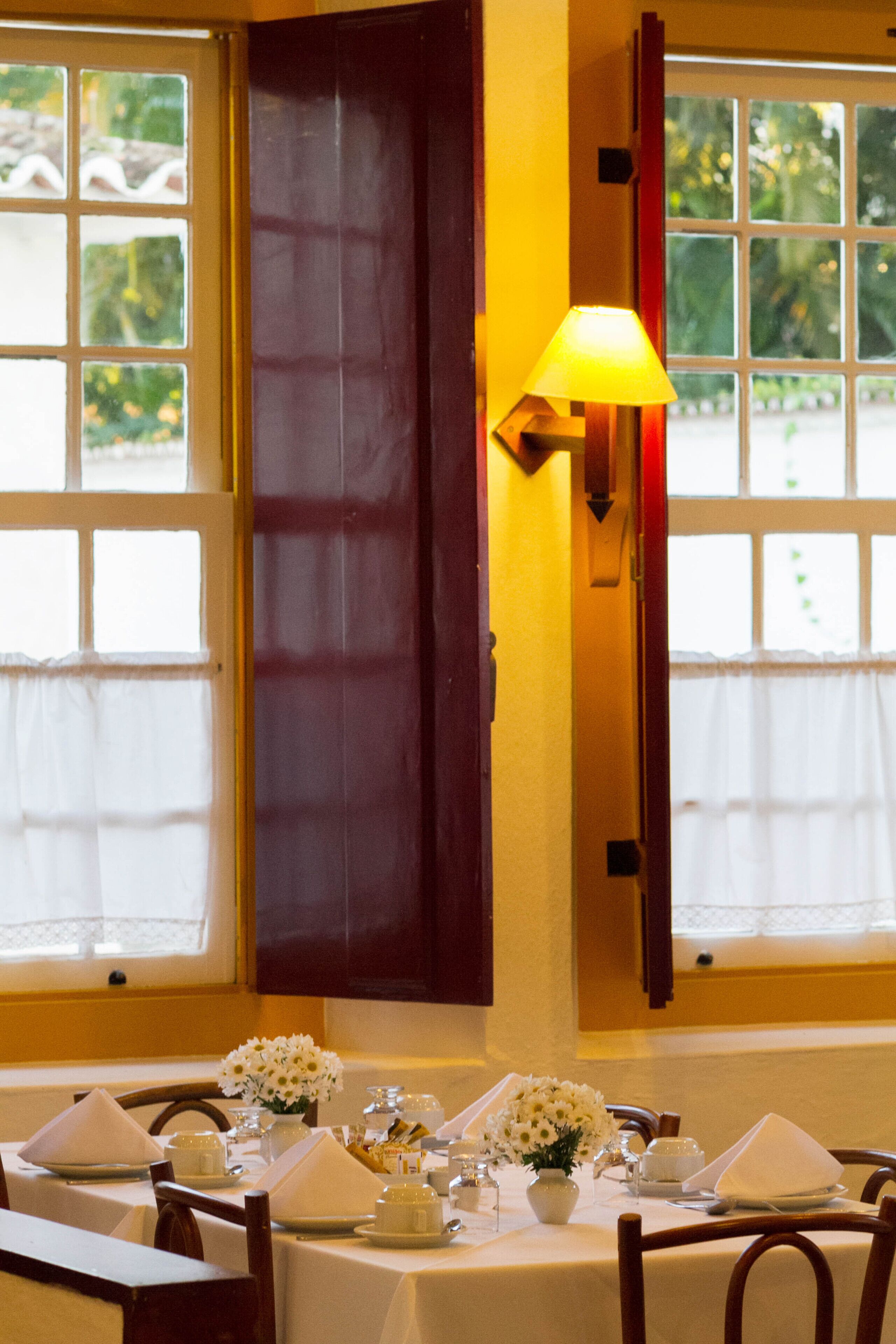 A dining area with a table set for four, a vase of flowers, and a lamp.