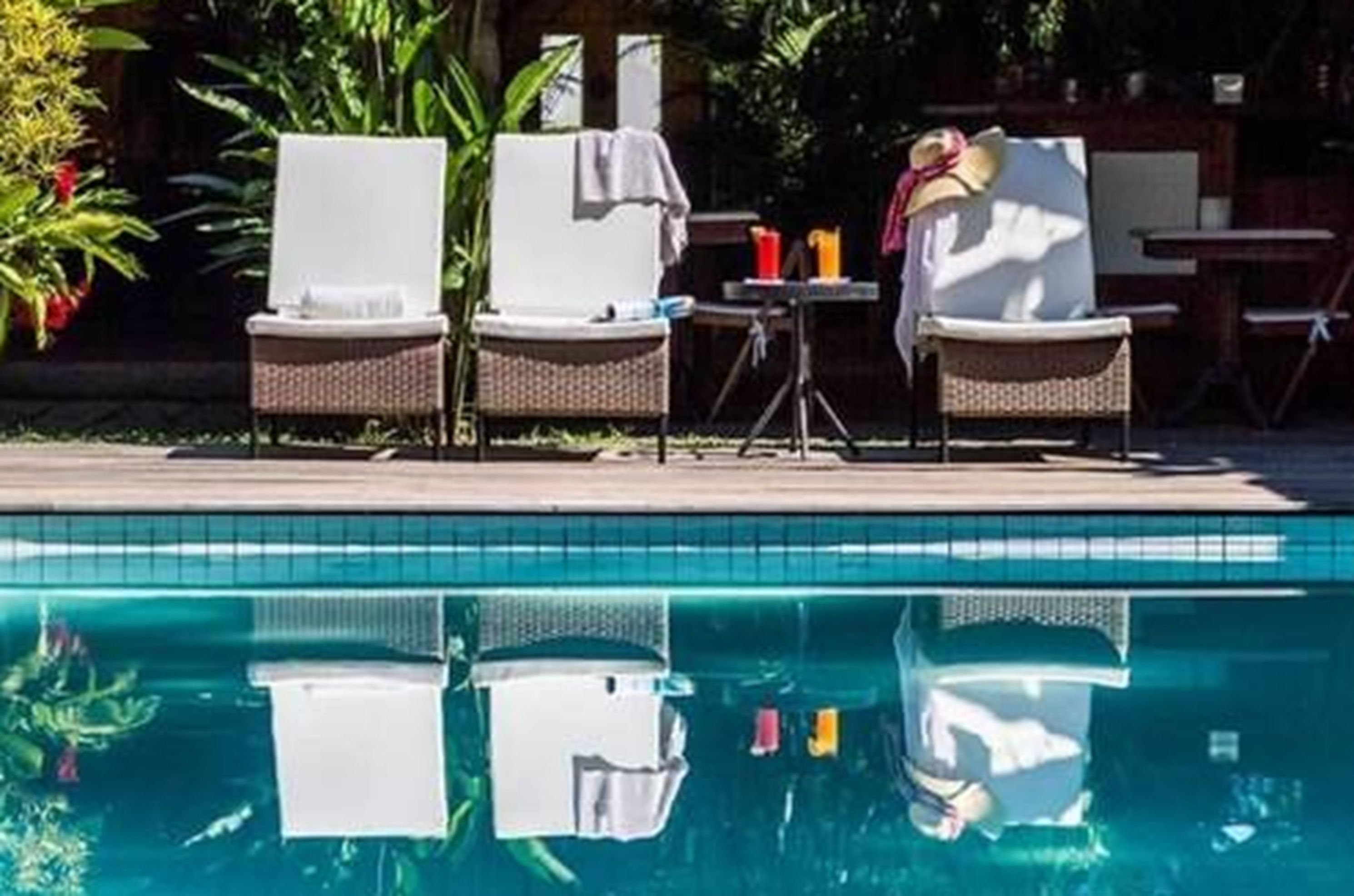A poolside area with lounge chairs and a table, surrounded by greenery.
