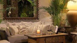 Un coin salon confortable avec un canapé moelleux, une table en bois ornée d’une bougie, des verres à vin et une bouteille.