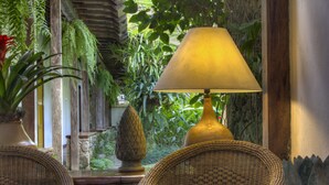 Une pièce meublée de mobilier en osier, avec une lampe et de nombreuses plantes d’intérieur.