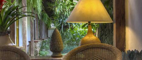 A room with wicker furniture, a lamp, and lush indoor plants.