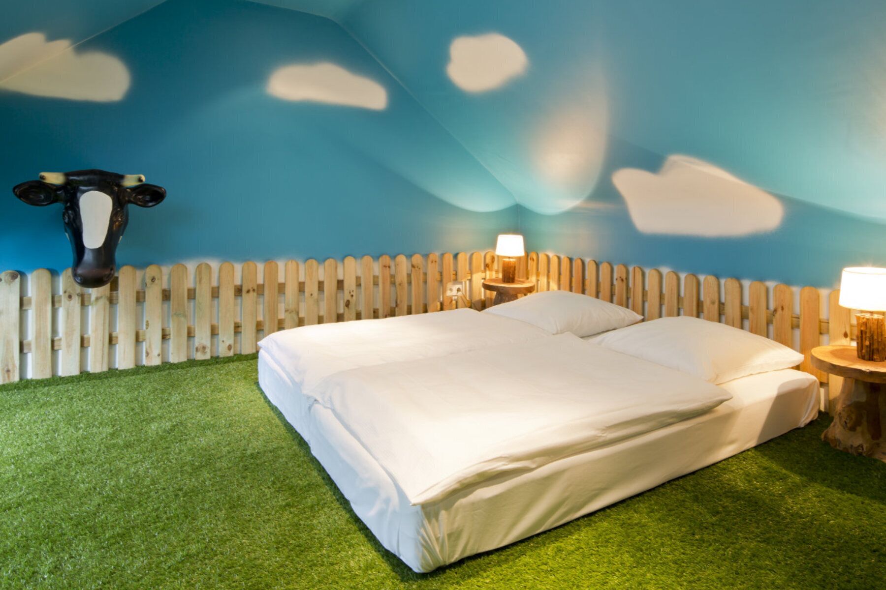 Una habitación con una cama, dos mesitas de noche, una valla de madera y una decoración de cabeza de vaca en la pared.