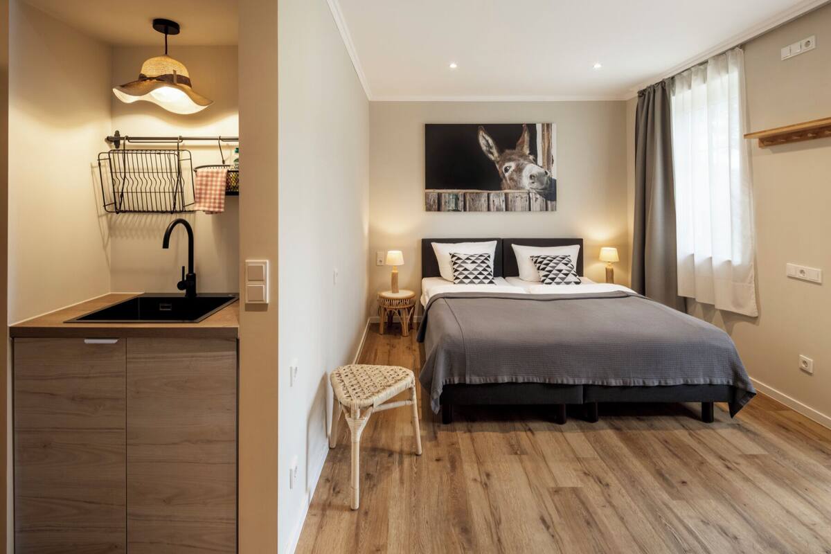 Un dormitorio moderno con una cama grande, un taburete pequeño, un lavamanos empotrado en la pared y una lámpara colgante.