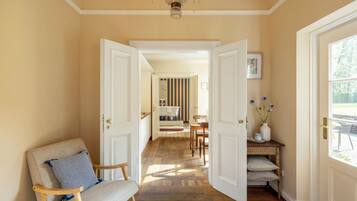 A hallway with a wooden rocking chair, a chandelier, and a view into a dining area.