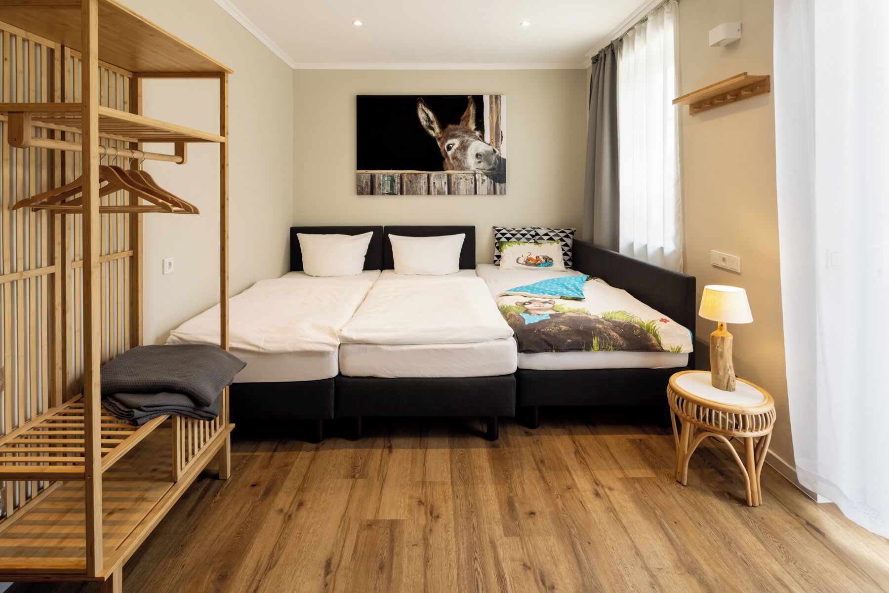 A bedroom with a bed, a wooden wardrobe, a wall-mounted painting, a bedside lamp, and a window with curtains.