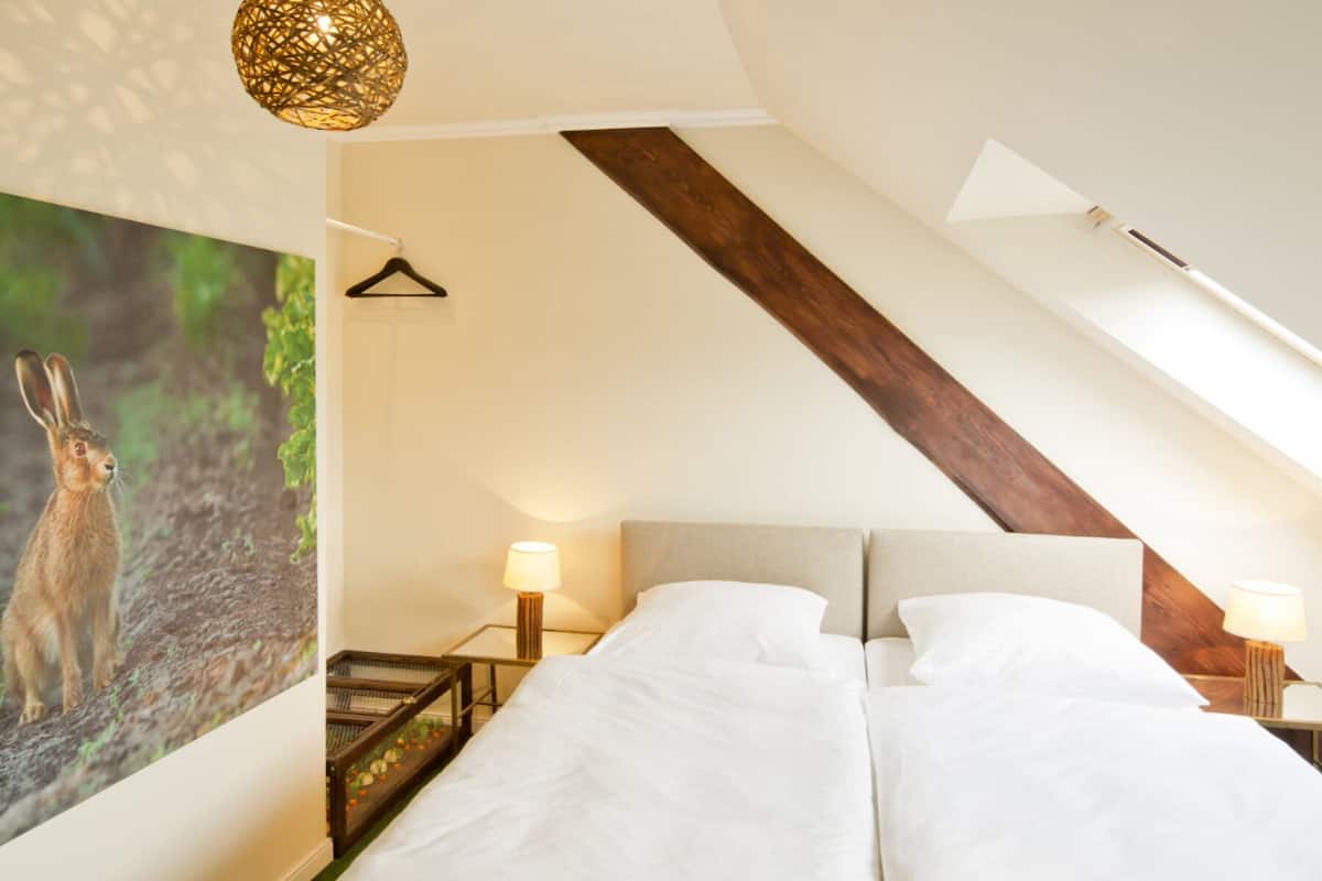 Un dormitorio con una cama, lámpara colgante, mesita de noche con lámpara y estante en la pared.