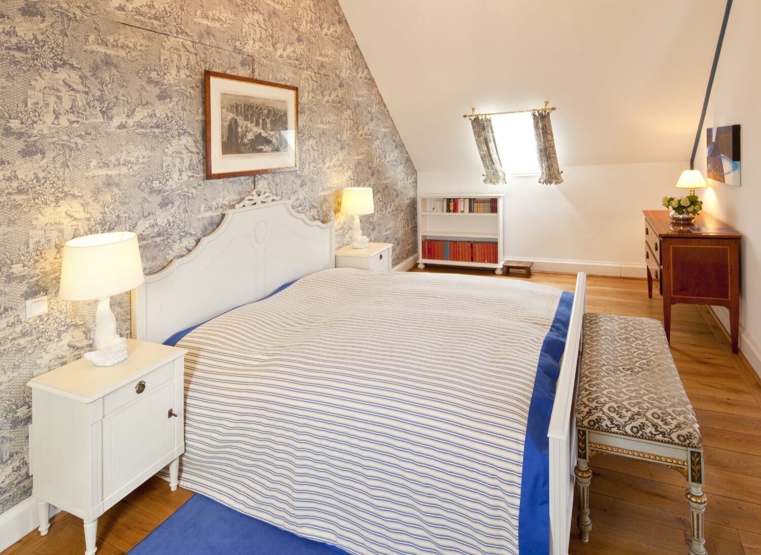 Un dormitorio con cama, mesitas de noche, una estantería, un banco y una pared de piedra con un cuadro enmarcado.