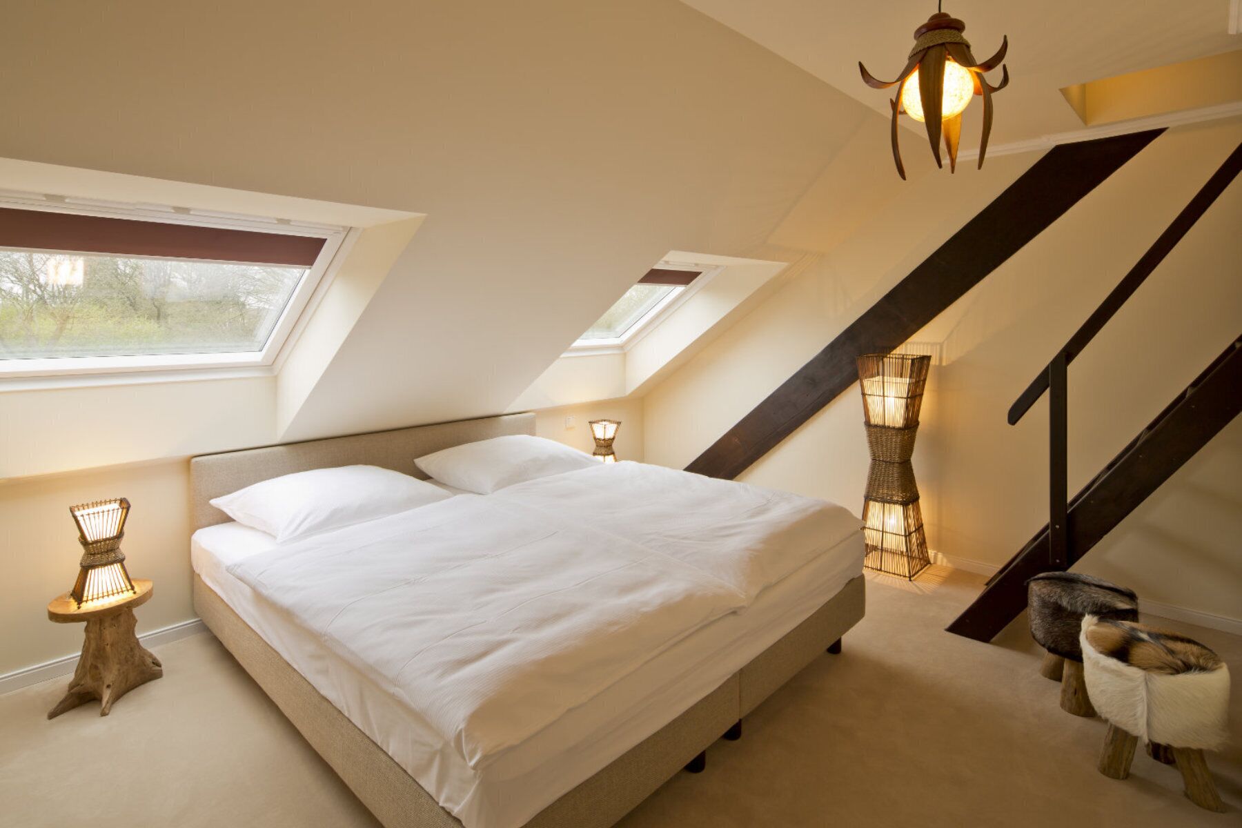 Un dormitorio con una cama grande, dos lámparas de noche, un tragaluz y una escalera de madera.